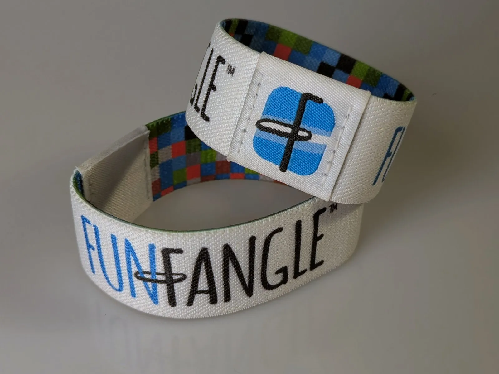 Two woven stretch fabric FunFangle wristbands, one showing the printed logo and one the patterned lining